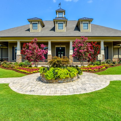 Exterior view showcasing Legacy at Jones Farm leasing office surrounded by meticulously maintained flowers, bushes, trees, and grass.