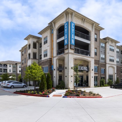 Exterior corner view of Cyan Craig Ranch apartments in McKinney, TX with their sign hanging on the second level and the leasing office on the ground floor