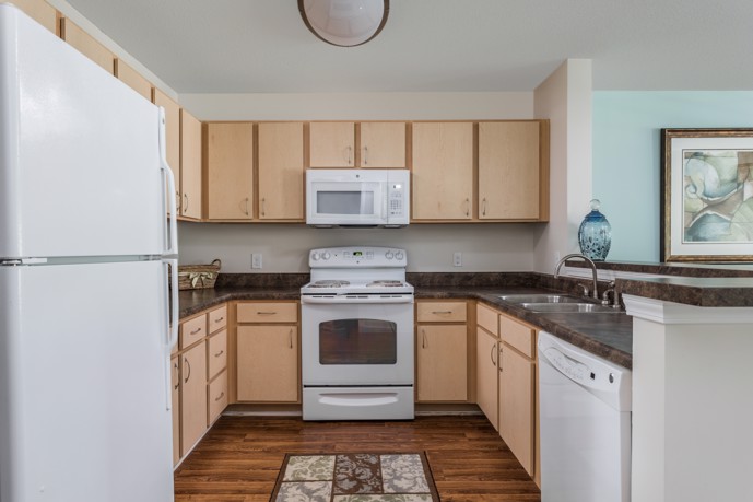 A modern kitchen boasting light wood-style cabinets, sleek granite countertops, and pristine white appliances, offering residents a stylish and functional culinary space at The Tides of Calabash.
