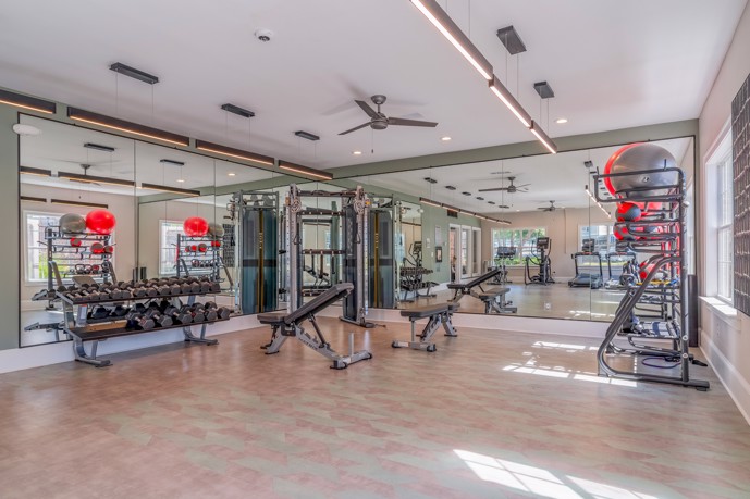 Fitness center equipped with weight equipment, fitness balls, large mirrors, and ceiling fans.
