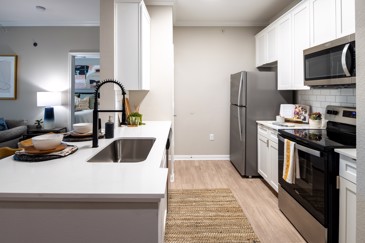 A galley kitchen at The Pointe at Vista Ridge features stainless steel appliances, quartz countertops, and white cabinets, combining modern style with functionality.