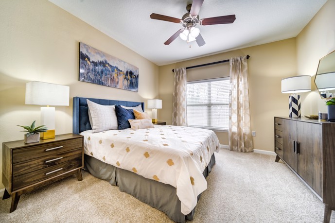 within an apartment at Waterstone at Brier Creek a queen bed adorned in a carpeted bedroom, flanked by generous large windows and an elegant armoire, creates a cozy retreat.