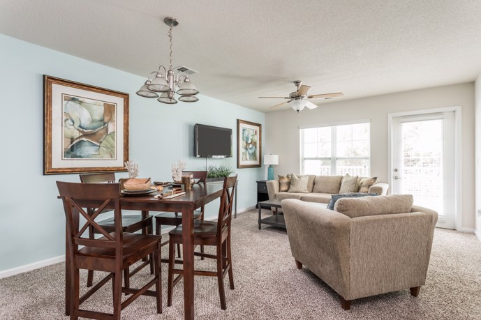 A comfortable carpeted living room furnished with a dining table and inviting living room furniture, providing residents with a cozy and functional space for relaxation and entertainment at The Tides of Calabash apartments.