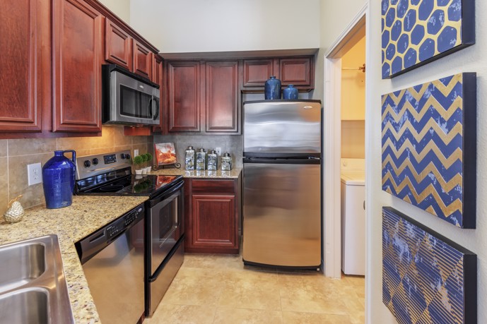 A modern kitchen equipped with stainless steel appliances, tiled flooring, elegant granite countertops, and a practical double-basin sink.