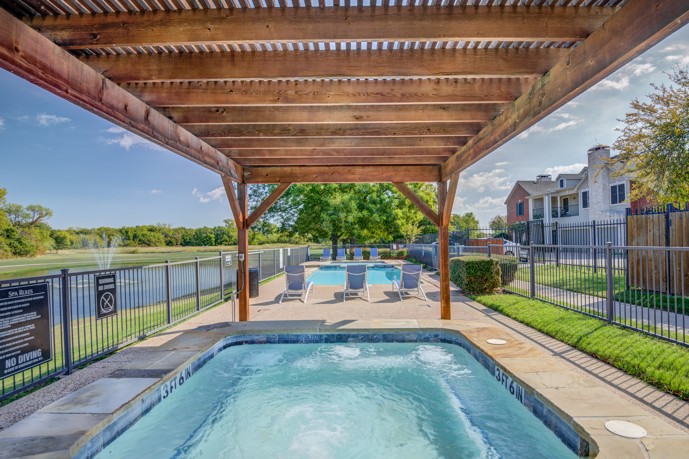 Two inviting swimming pools with a sundeck, pergola covering, and lounge chairs nestled near a serene pond.