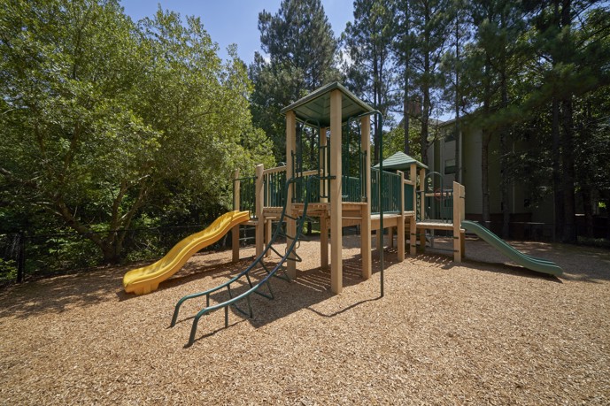 Onsite playground at Sugar Mill apartments with mulch and trees in the background. 