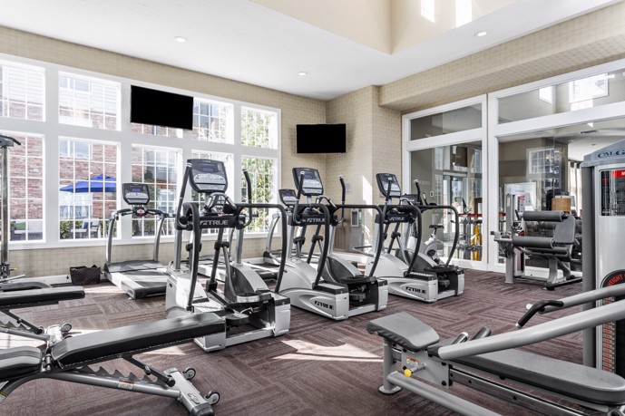 The carpeted fitness center at The Chelsea apartments in Columbus, Ohio, boasting large windows that flood the space with natural light and a diverse selection of gym equipment for residents' workouts.