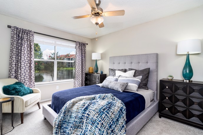 A tranquil carpeted bedroom adorned with a queen bed, offering picturesque views of the serene lake through the window and complete with two bedside tables, providing residents with a peaceful sanctuary within the Vantage on Hillsborough apartments.