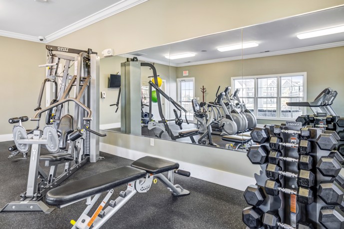 Close-up view of exercise equipment and dumbbells in front of a long mirror at an apartment community fitness center