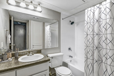 A pristine bathroom with white tile, a white vanity, a large mirror, and one sink at Vue at Knoll Trail.