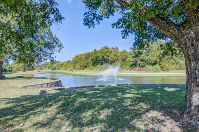 A sprawling pond with a graceful fountain, embraced by verdant trees and verdant grass at Lakeside at Coppell.