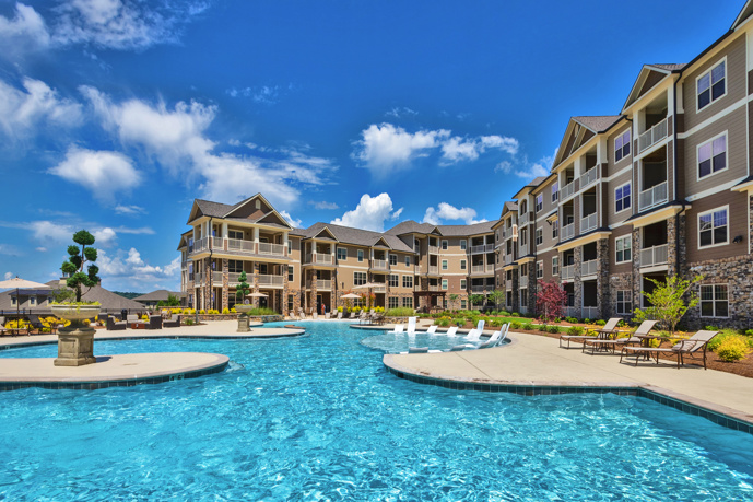 Inviting saltwater swimming pool featuring submerged lounge chairs, a spacious sundeck, and lush bushes near Legacy at Jones Farm apartments.