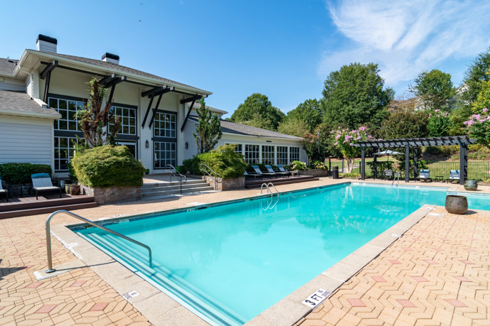Outdoor community apartment swimming pool surrounded by a fence with trees and a lake on the other side
