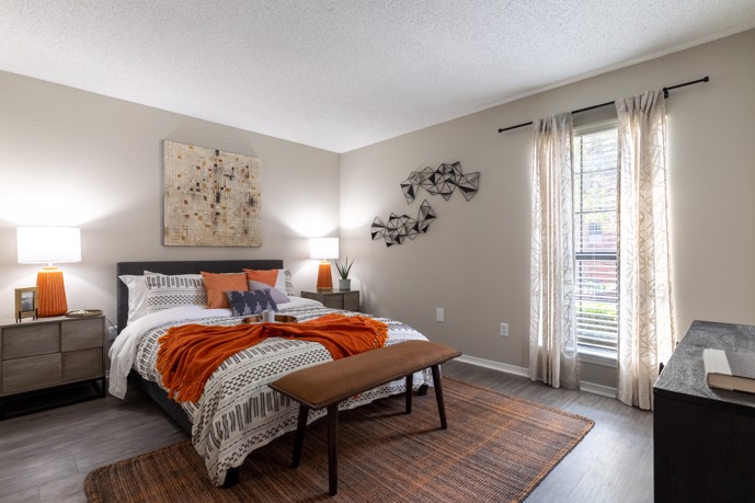 A cozy bedroom exuding comfort and relaxation, complete with wood-style flooring, a generously sized window allowing natural light to filter in, and a plush queen bed at The Augusta.