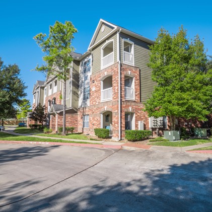 Exterior corner view of the Carrington Place apartments with a street in the foreground and trees along the side of the building