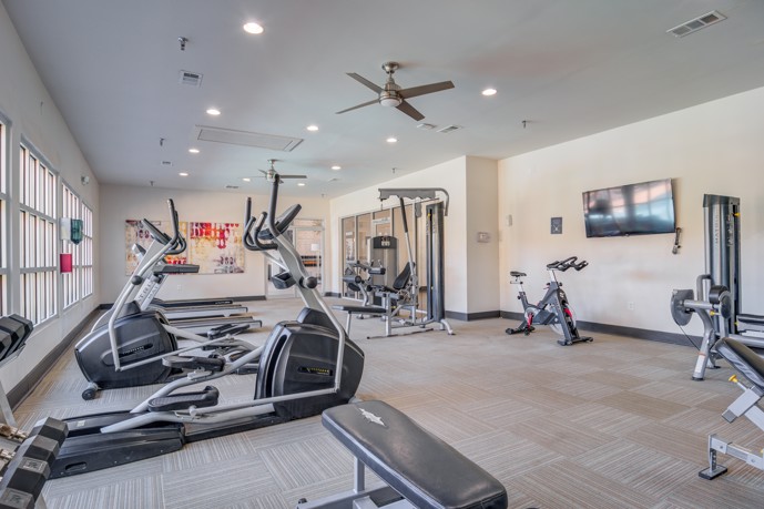 Community fitness center with exercise equipment along the walls, recessed ceiling lighting, and ceiling fans