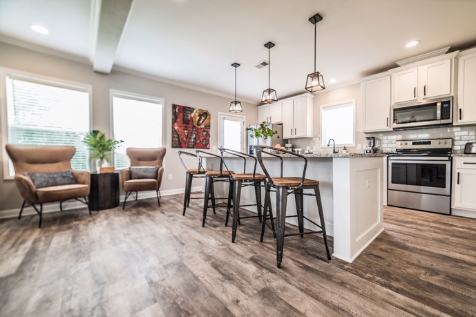 A stylish apartment at Virtuoso apartments in Huntsville, AL, featuring wood-style flooring and an open floor plan that includes a kitchen with a granite counter bar.