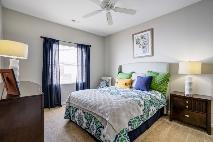 Comfortable bedroom featuring a ceiling fan, plush carpeting, and a window with natural light, ensuring a peaceful retreat.