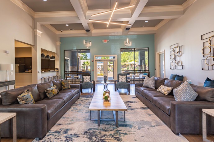 The contemporary clubhouse at Waterstone at Brier Creek features large windows allowing ample natural light, two inviting couches for seating, and a kitchen area designed for entertaining.