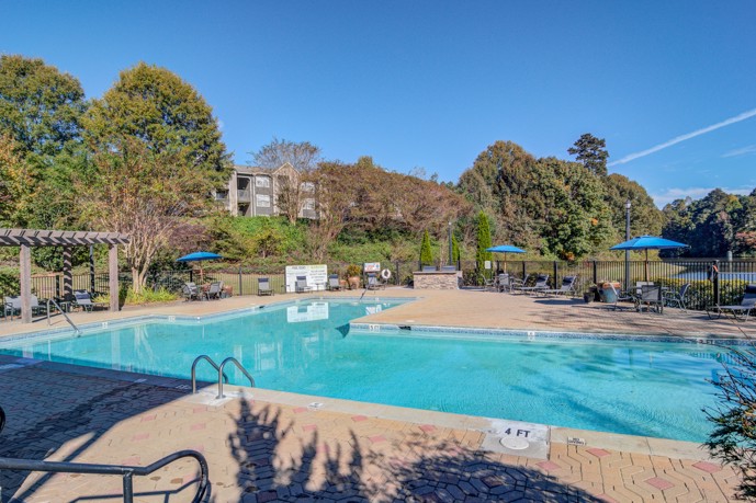 Large T-shaped outdoor swimming pool with trees and a lawn in the background at 1250 West apartments in Marietta, GA 