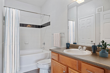 Apartment bathroom with a wooden vanity, large mirror, toilet, and a black-and-white tiled tub