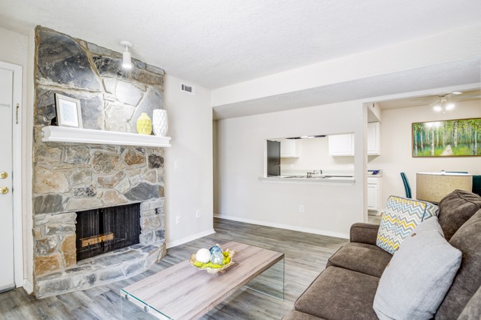An apartment living room at Windrush with a stone fireplace, wood-style flooring, and a dining area and kitchen nearby. 