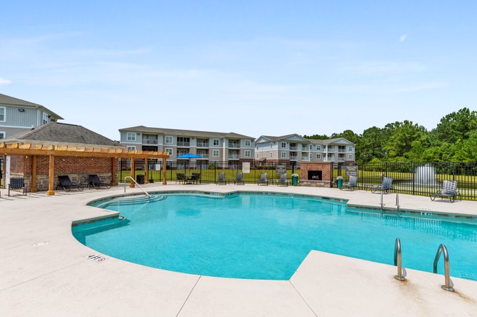 At The Tides of Calabash, a luxurious resort-style pool featuring a sitting area with a fireplace, nestled amidst the elegant architecture of the apartments, providing residents with a serene outdoor retreat.