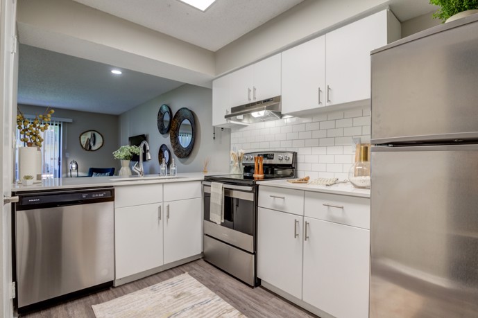 A sleek and modern kitchen at The Invitational, boasting pristine white cabinets, gleaming stainless steel appliances, and a seamless flow into the adjacent dining area.