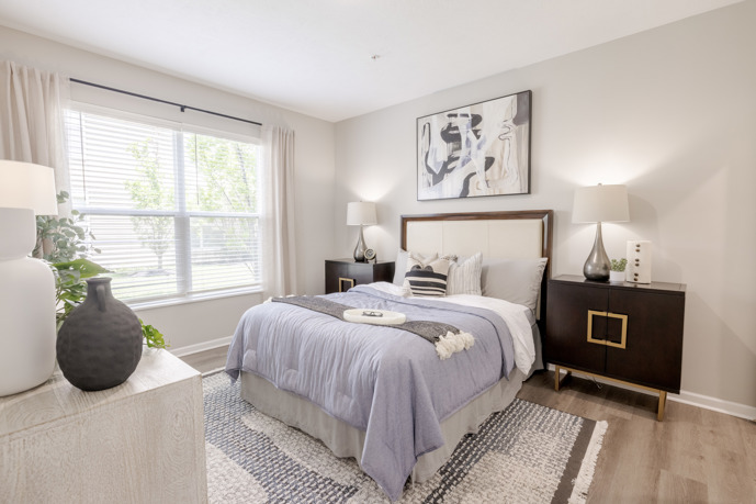 A cozy bedroom adorned with a queen bed, windows allowing natural light to fill the space, and two bedside tables, providing a comfortable haven at The Chelsea.