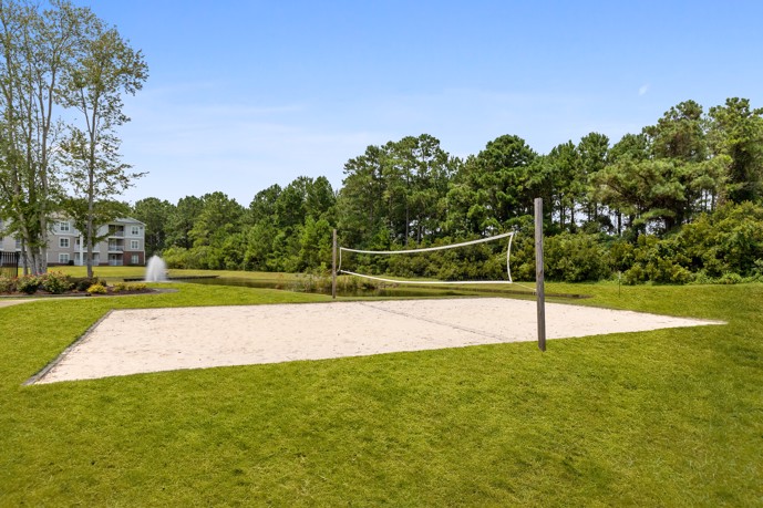 A vibrant volleyball court enveloped by lush vegetation, offering residents a picturesque setting for recreational activities at The Tides of Calabash apartments.
