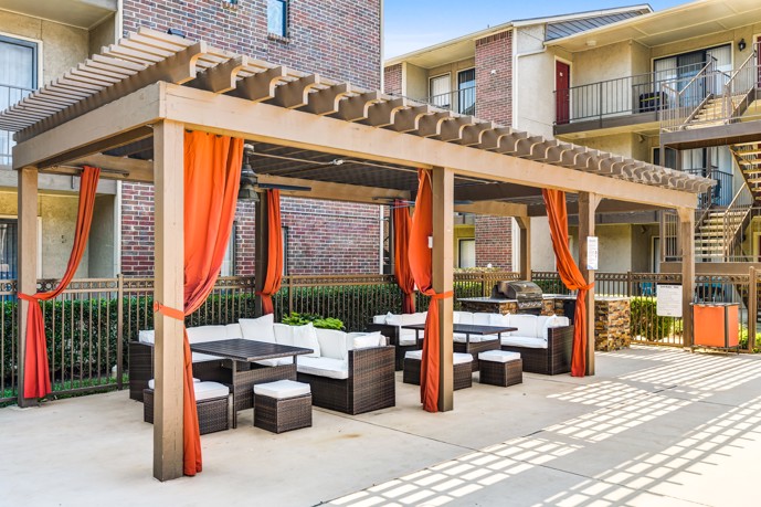 At Vue at Knoll Trail in North Dallas, Texas, the outdoor Pergola is a true oasis, featuring comfortable lounge seating and tastefully adorned with vibrant orange curtains, creating a perfect spot for relaxation and rejuvenation.