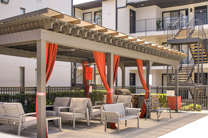 At Vue at Knoll Trail in North Dallas, Texas, the outdoor Pergola is a true oasis, featuring comfortable lounge seating and tastefully adorned with vibrant orange curtains, creating a perfect spot for relaxation and rejuvenation.