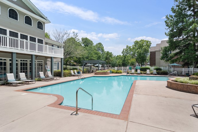 Inviting swimming pool area with comfortable lounge chairs, umbrellas, and lush trees, adjacent to the clubhouse at North Park at Eagles Landing.