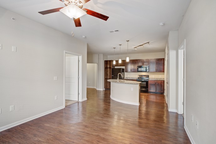A spacious open kitchen and living room with beautiful hardwood floors and ceiling fan. 