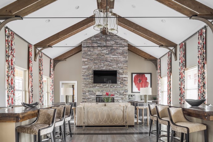 Long view facing a fireplace with a sofa in front of it in the Aston apartments community clubhouse that has a vaulted ceiling and chairs along both sides of the room