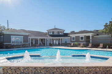 Large in-ground hot tub with three small fountains in it, a large pool behind it, and apartment buildings behind the pool