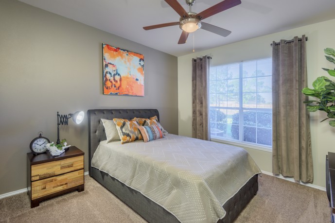 Tranquil bedroom adorned with a spacious window, cooling ceiling fan, and plush carpet flooring.