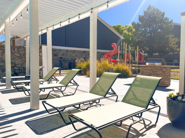 A spacious outdoor pool area with lounge chairs, umbrellas, and lush landscaping, perfect for relaxation and enjoying sunny days at Windrush in Oklahoma City, OK.