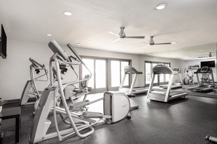 Black and white photo of the Bennington Pond apartments fitness center with exercise equipment and a flat screen TV