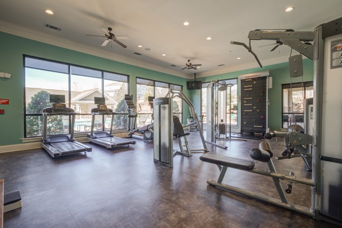 A well-equipped fitness center at Waterstone at Brier Creek, featuring ample natural light streaming in through large windows and a wide array of gym equipment, offering residents an energizing space for workouts.