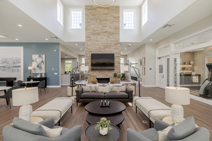 A spacious clubhouse adorned with various seating options, a pool table, TVs, and a well-equipped kitchen area, creating a welcoming atmosphere at The Chelsea apartments.