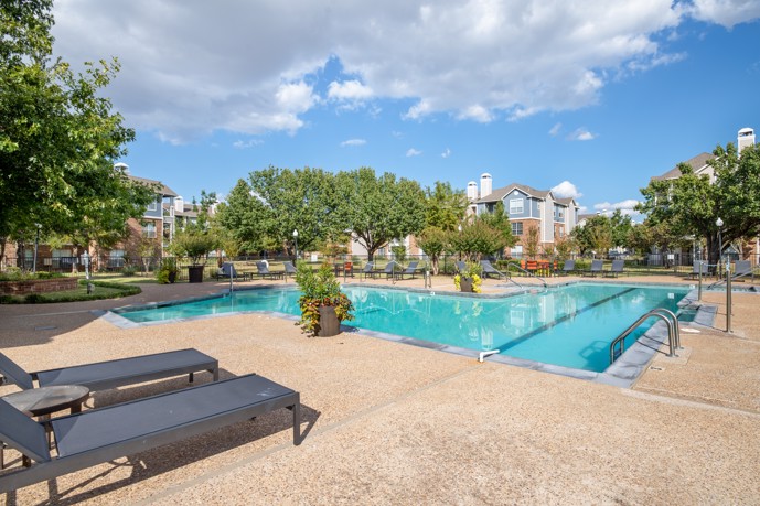 Inviting swimming pool area with comfortable lounge chairs, vibrant flower pots, and a backdrop of lush trees and apartment buildings at Montclair Parc.