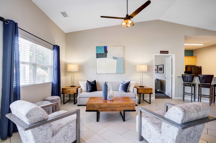 Clubhouse featuring a comfortable seating area, well-appointed community kitchen, and elegant tile flooring, offering a welcoming space for residents.