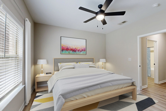 A bedroom in an apartment at Waterstone Big Creek boasts wood-style flooring, a ceiling fan, and tasteful furniture.