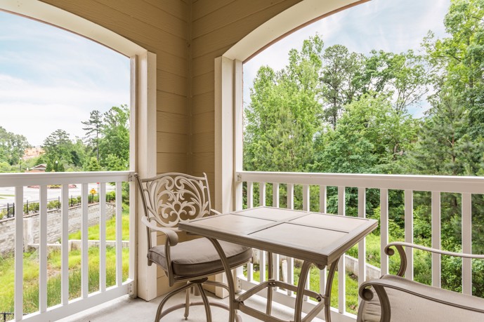 A balcony adorned with a table and chairs, offering serene views of surrounding trees and providing a peaceful outdoor space for relaxation and dining at Waterstone at Brier Creek apartments in Raleigh, NC.