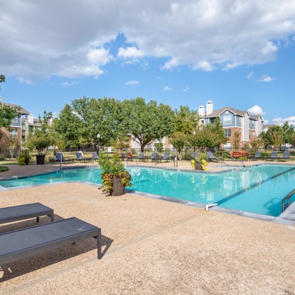 Serene swimming pool surrounded by lounge chairs, flower pots, and verdant trees, nestled amidst the apartment buildings at Montclair Parc.