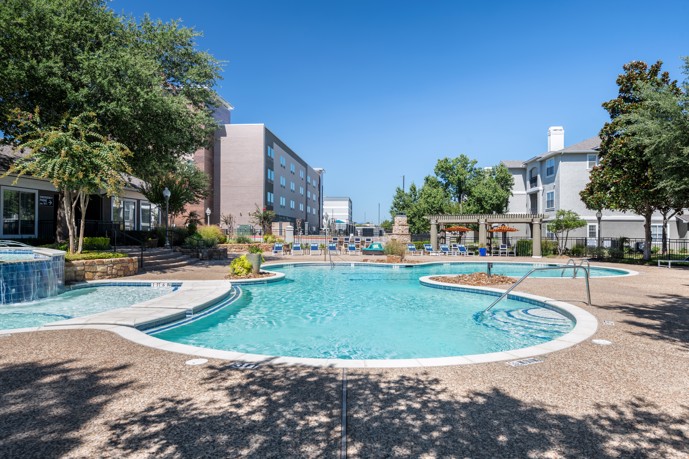 Swimming pool featuring a serene fountain, spacious sundeck, comfortable lounge chairs, umbrellas, and shaded pergola patios.