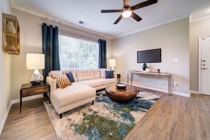 A cozy living room within Thornhill apartments, adorned with a comfortable two-seater couch, expansive windows allowing ample natural light, and stylish wood-style flooring, creating a warm and welcoming atmosphere.