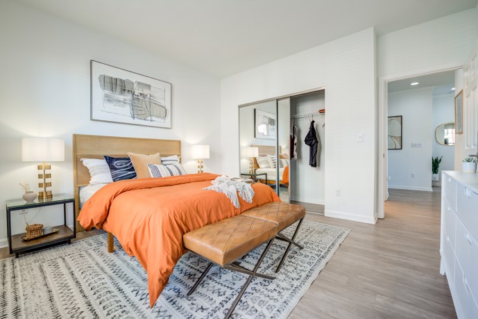 Calming apartment bedroom furnished with an orange bed, nightstands, and a leather bench