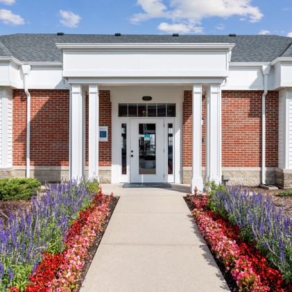 Welcoming entryway lined with flowers leading to the brick building housing Harrison Place clubhouse.